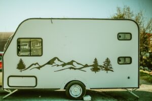 White small travel trailer with a dark mountain and pine tree decal on the side, parked on a sunny lot.