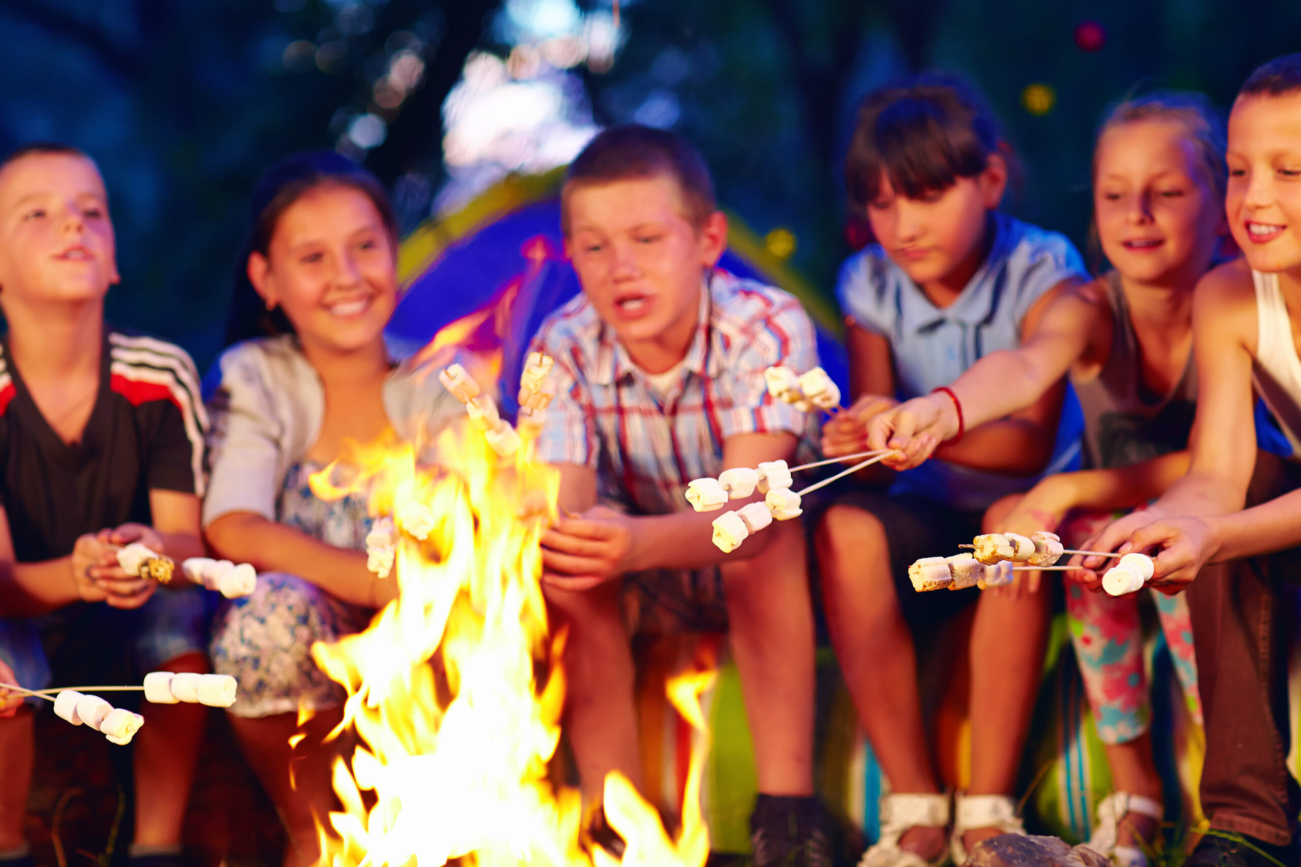 group of happy kids roasting marshmallows on campfire