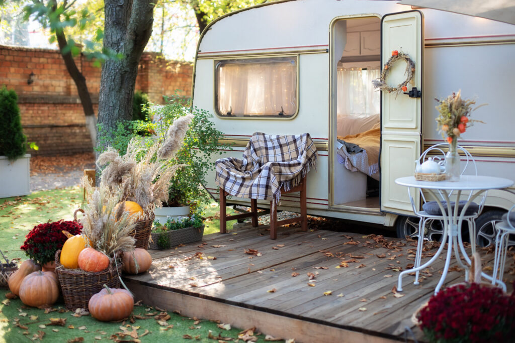 Wooden RV house porch with garden furniture Decor summer yard Campsite in garden Interior cozy yard campsite with green plants potted Wooden armchair with plaid near outside retro caravan trailer | I Heart RVing
