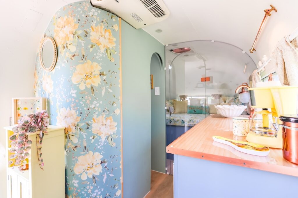 Rise2ShineAirstream2 | I Heart RVing Pastel-colored vintage camper interior with blue floral wallpaper, a peach countertop, and a compact kitchenette.