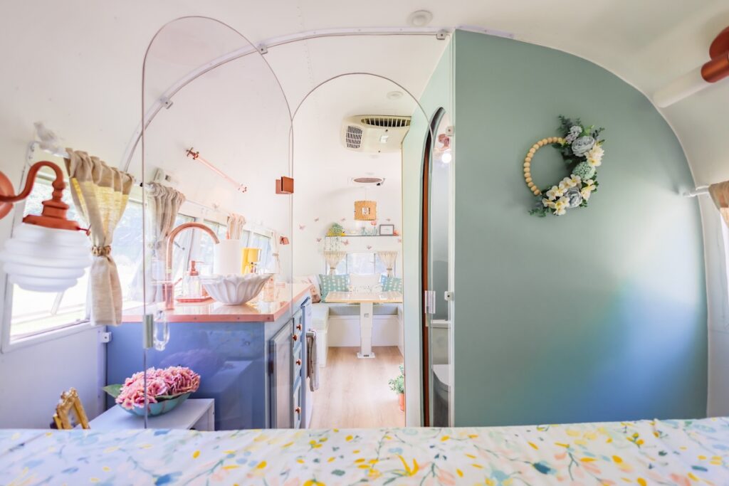 Rise2ShineVenturesAirstreamSprout | I Heart RVing Interior of a pastel vintage caravan with a blue kitchenette, sink, and cozy dining nook visible at the far end, decorated with soft curtains and flowers.